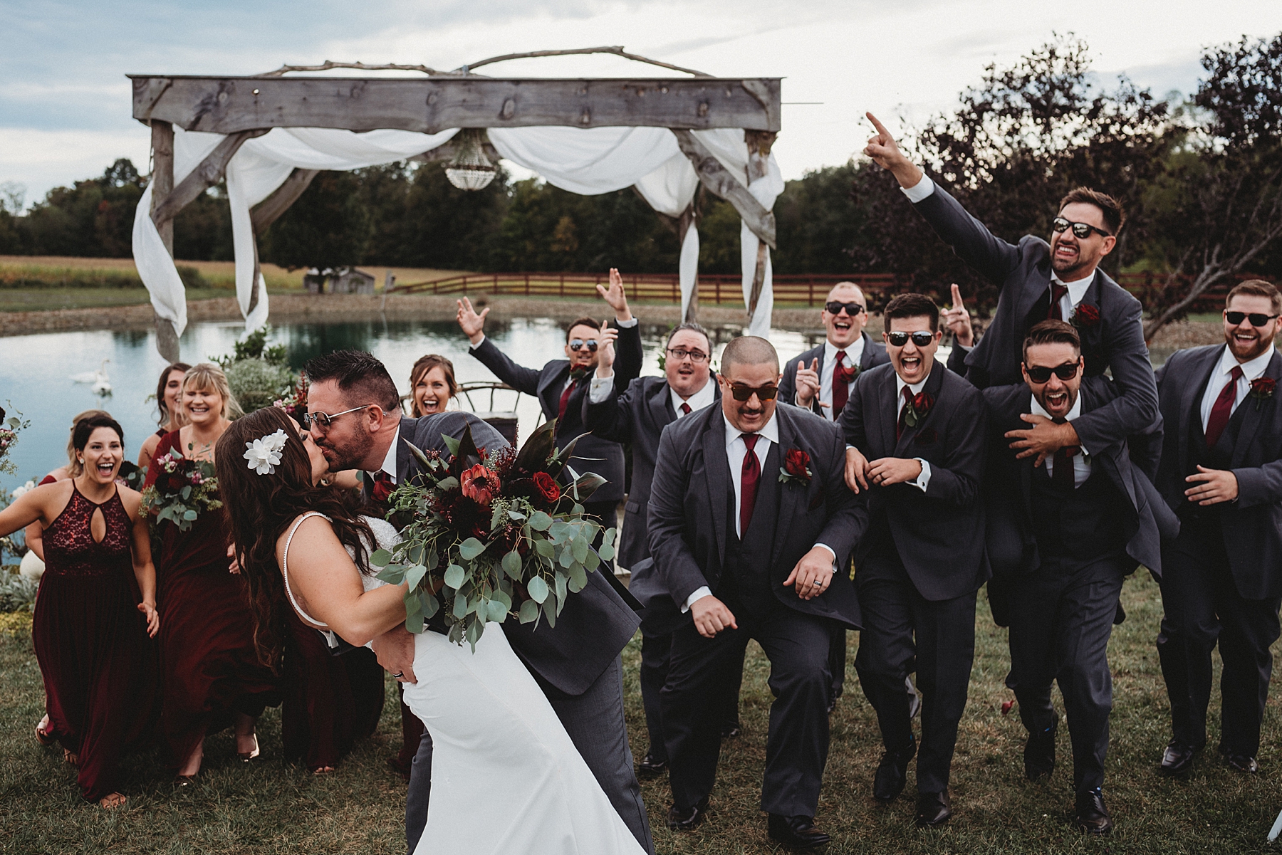 groom kisses his bride with his groomsmen in the background