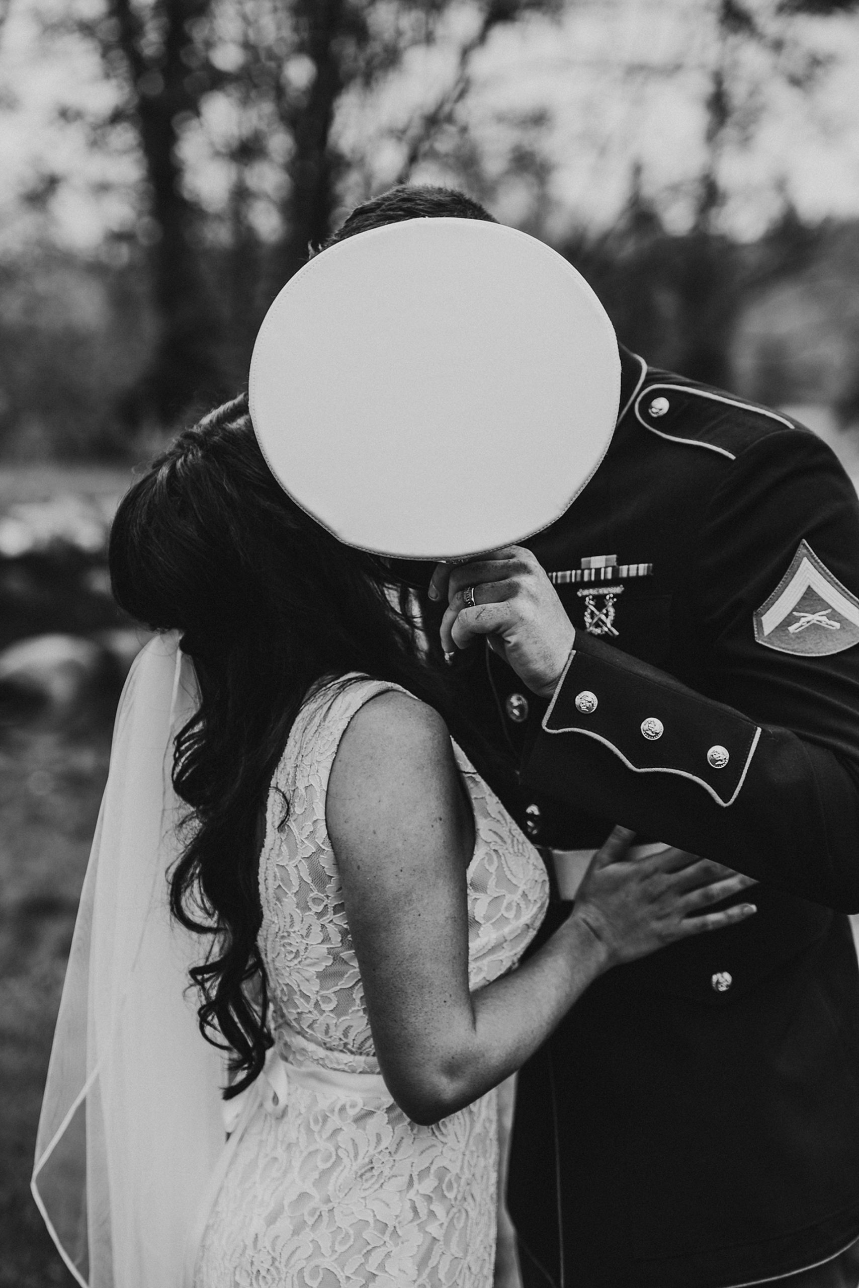 newlyweds kiss as groom holds up his hat to cover them 