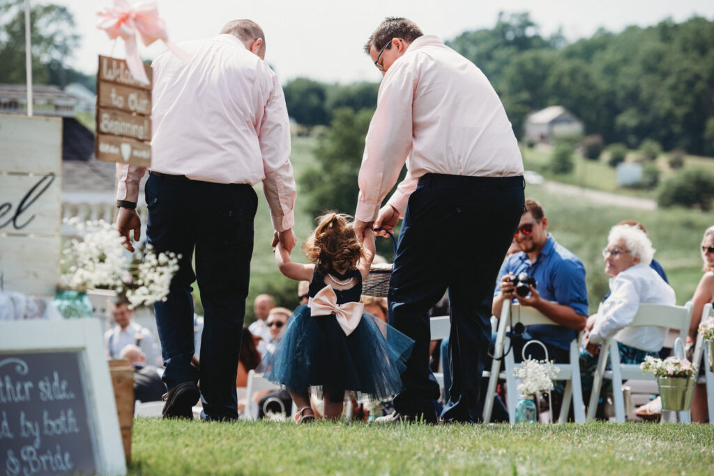 two men walking the flower girl down the aisle during their Amish Door wedding day