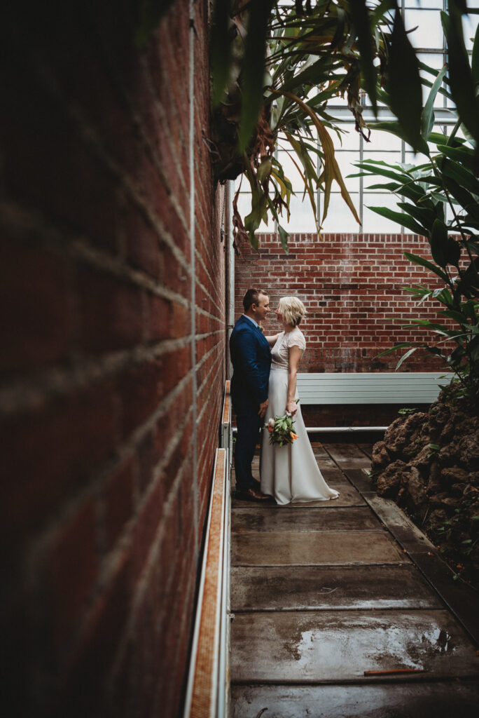 groom leaning against a brick wall with his bride Elope Ohio